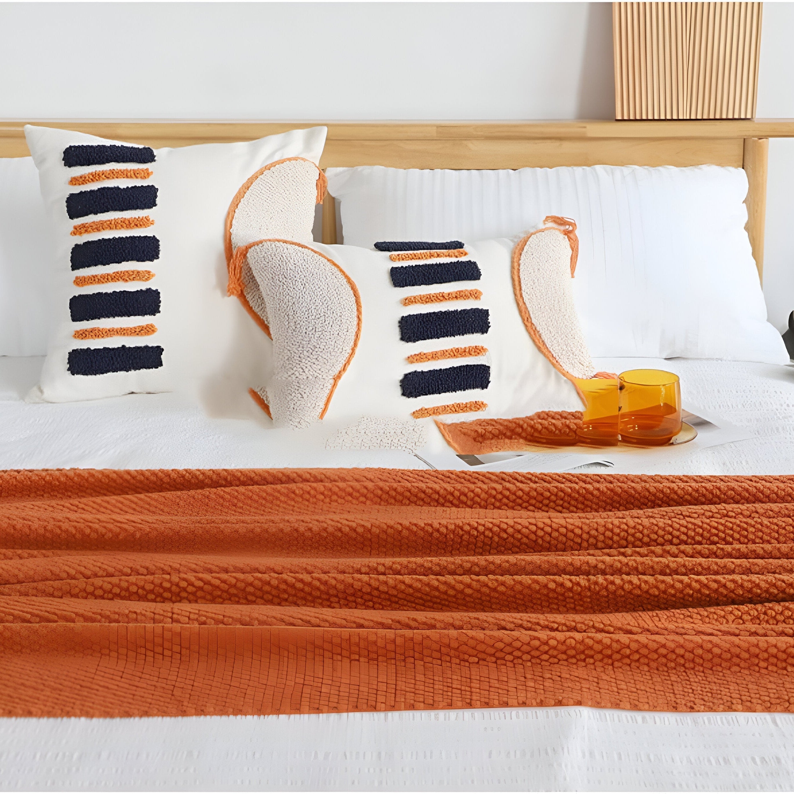 Decorative pillows with orange and blue patterns on a bed with an orange throw blanket.