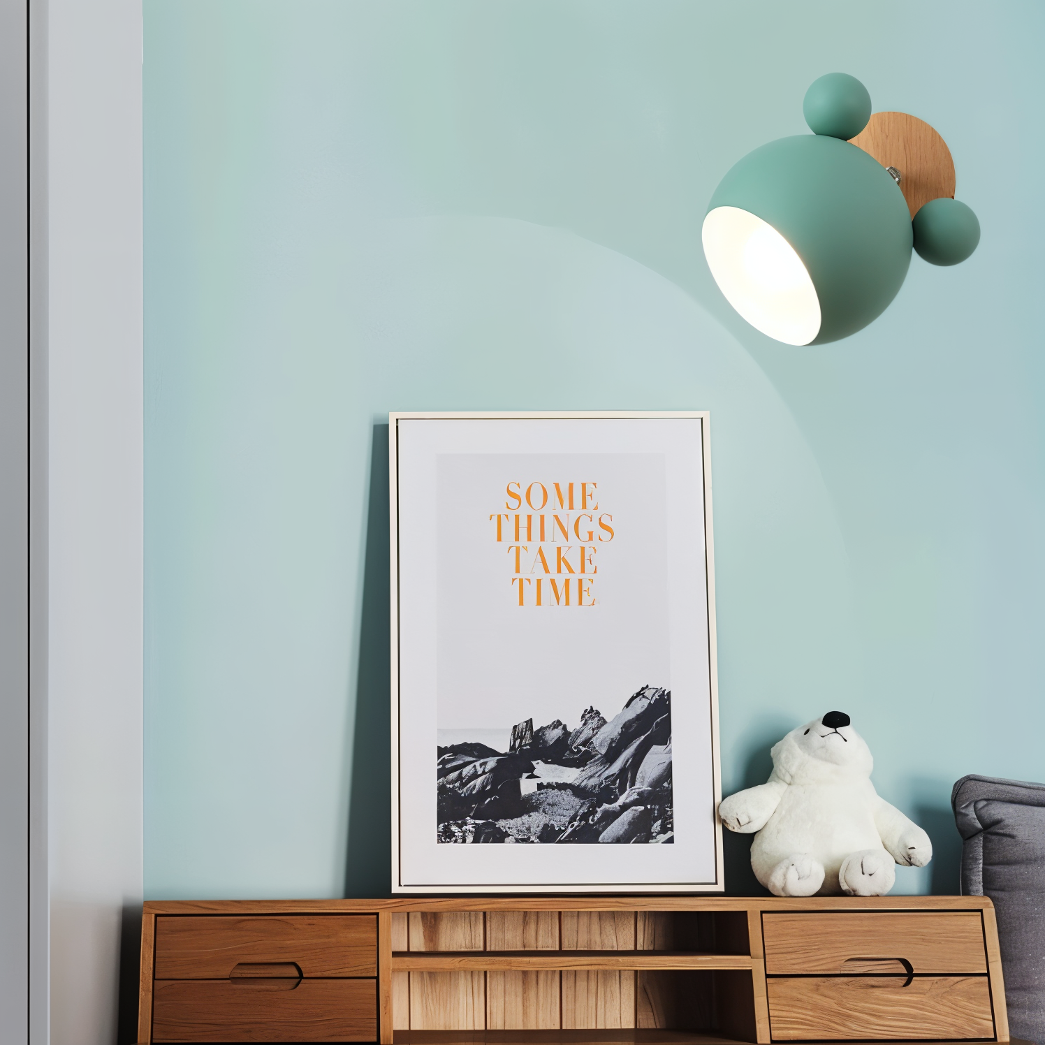 Framed artwork with text and a teddy bear on a wooden shelf against a light blue wall with a modern lamp.