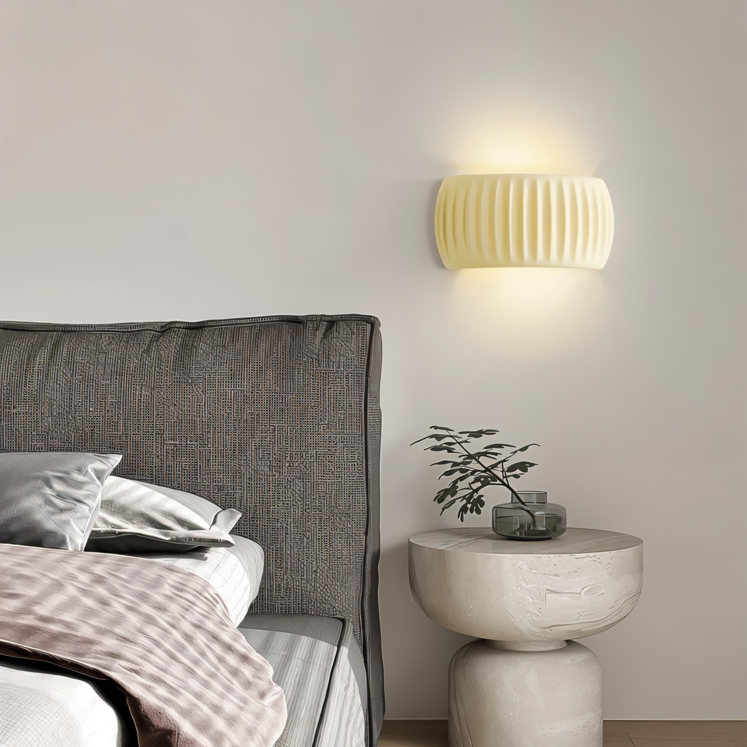 Bedroom with a gray upholstered headboard and a round stone side table with a plant and lamp.