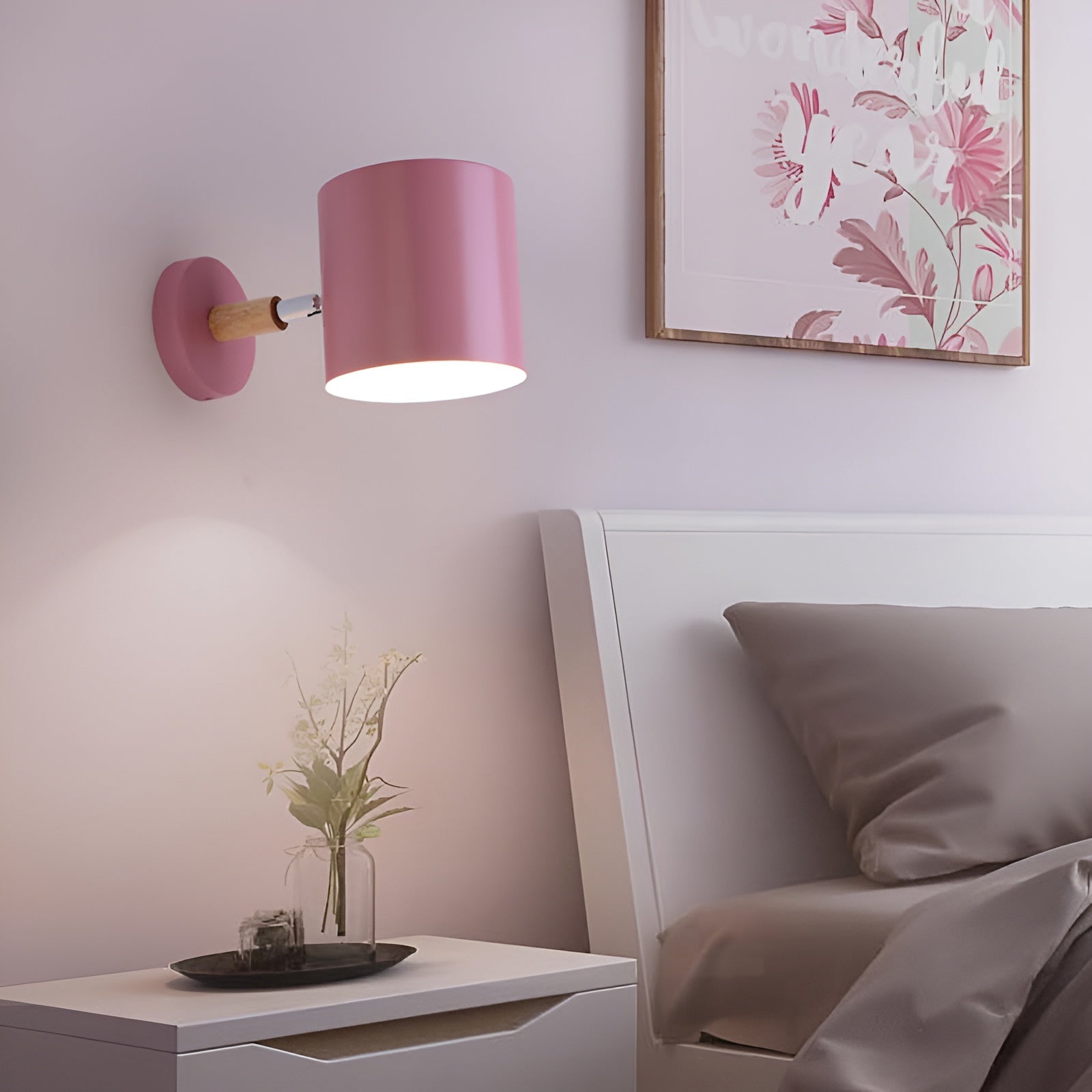 Pink wall lamp on a nightstand next to a bed with floral artwork on the wall.