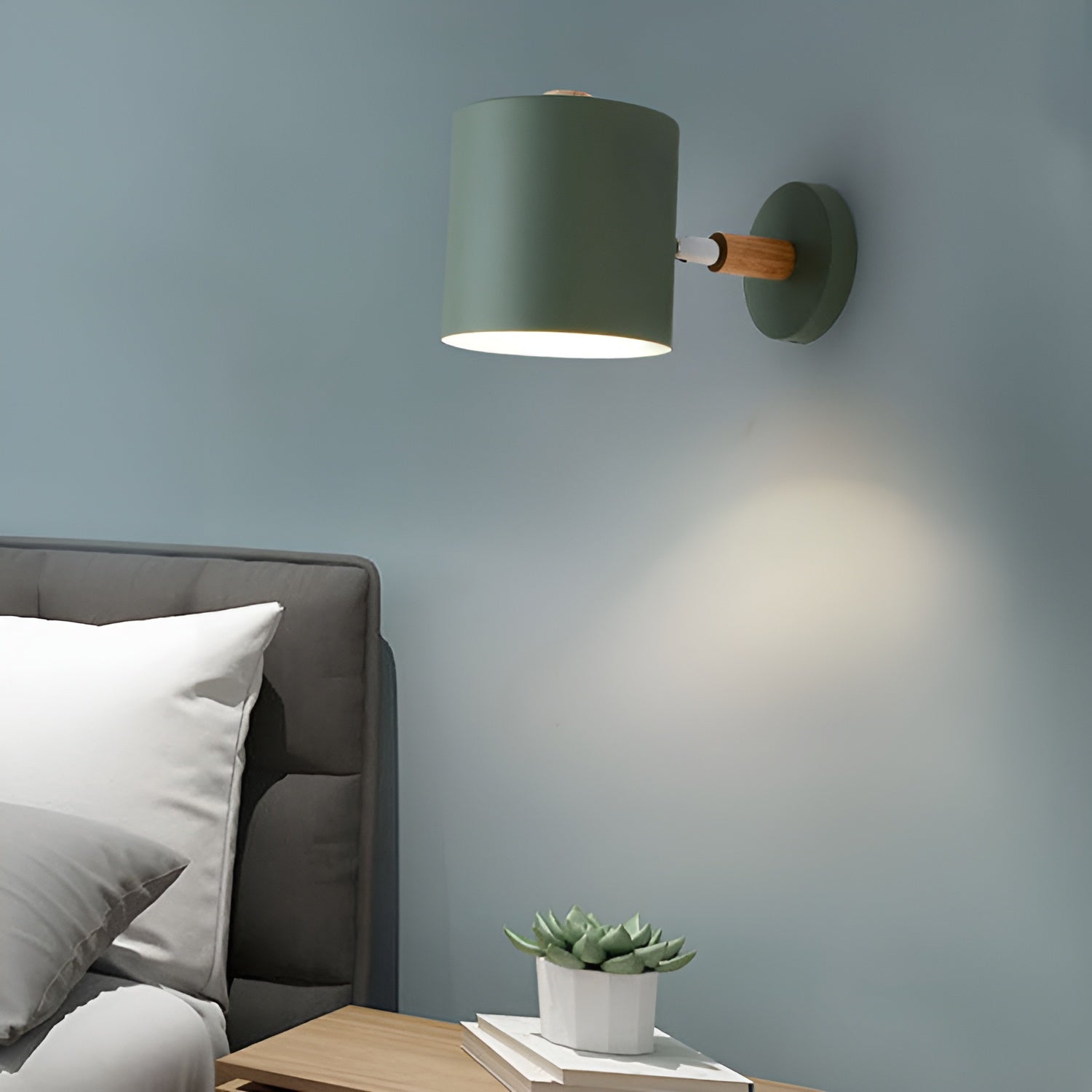 Green wall lamp on a gray wall with a bed and plant in the foreground