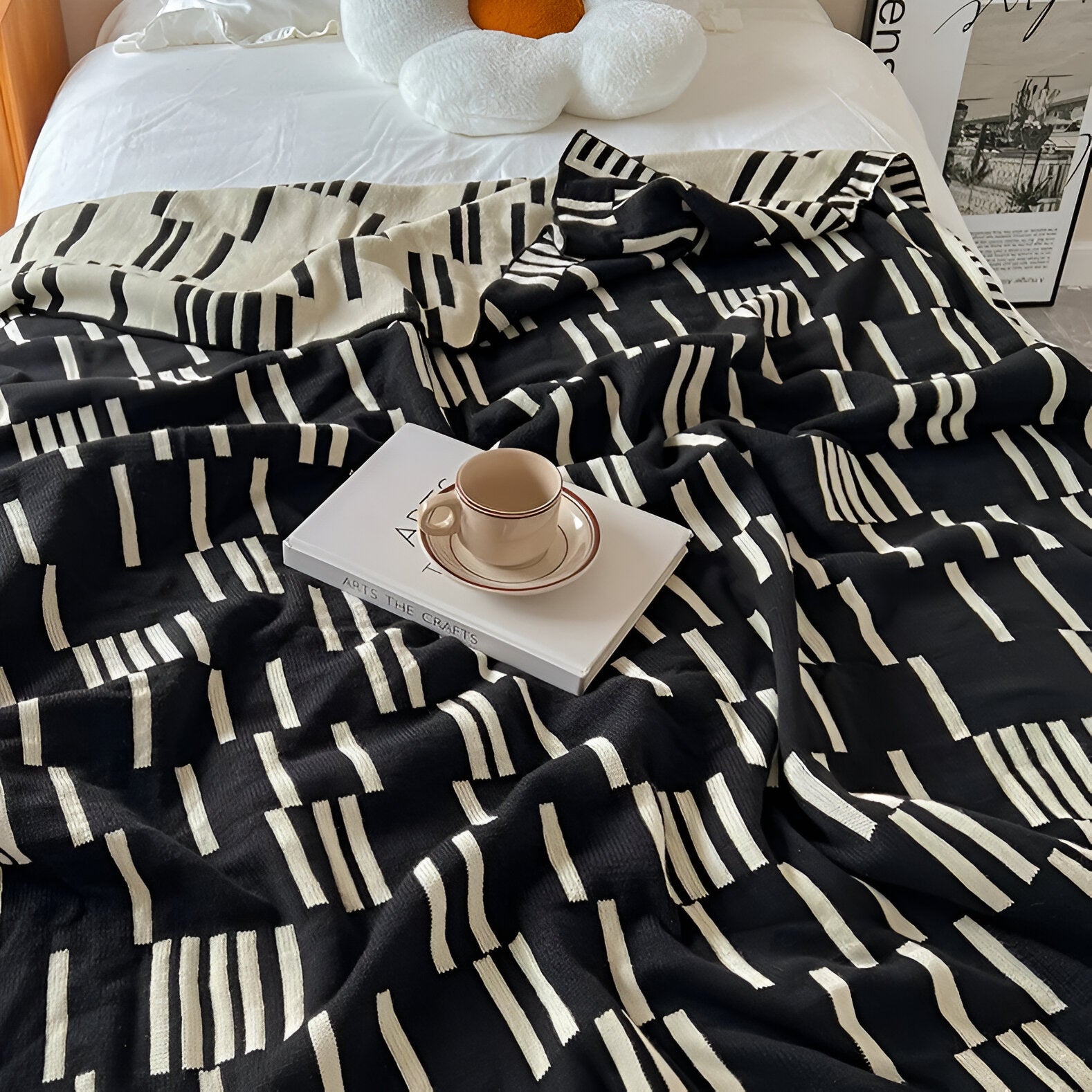 Black and white patterned comforter on a bed with a book and cup on top.