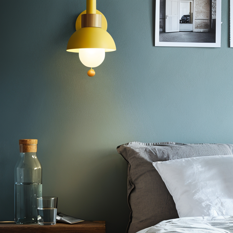 Yellow pendant light above a bed with a bottle and glass on a nightstand.