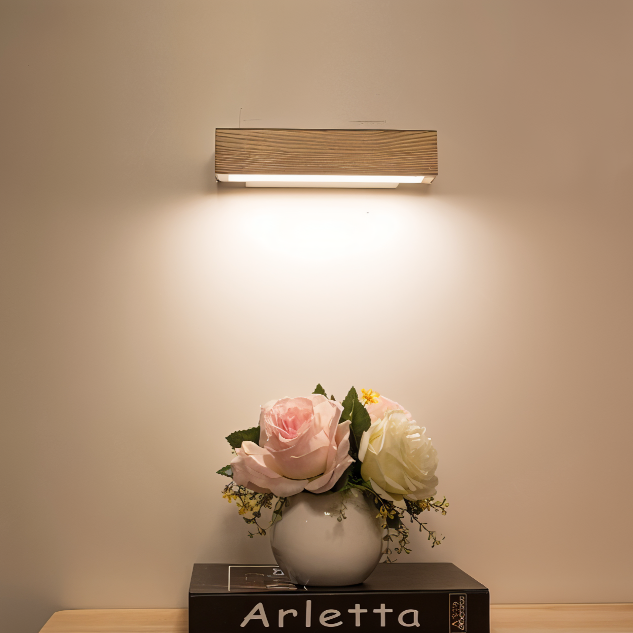 Wall-mounted light fixture illuminating a vase with flowers on a table.