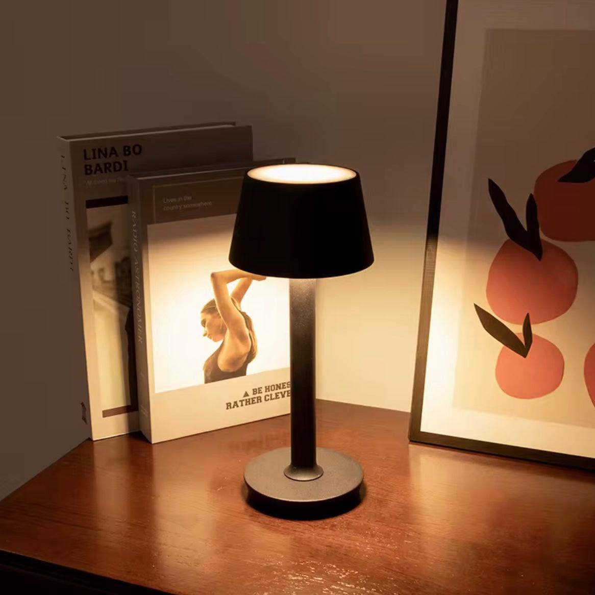 Black table lamp on a wooden surface with books and a framed picture in the background