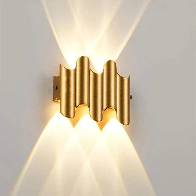 Gold wall sconce with wavy design on a white wall