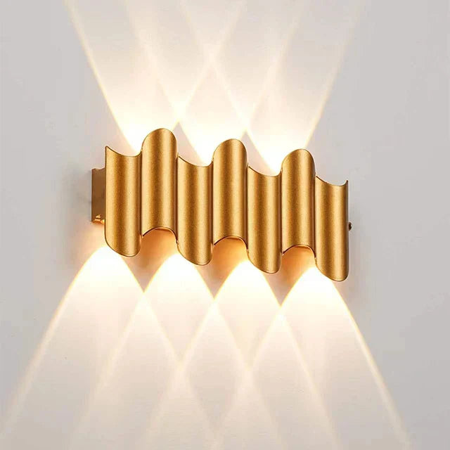 Gold wall-mounted light fixture with wavy design on a white background