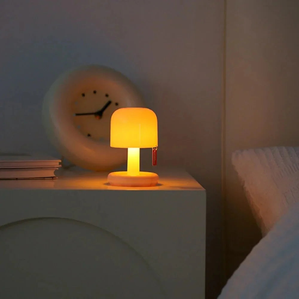Small orange lamp on a nightstand with a clock in the background