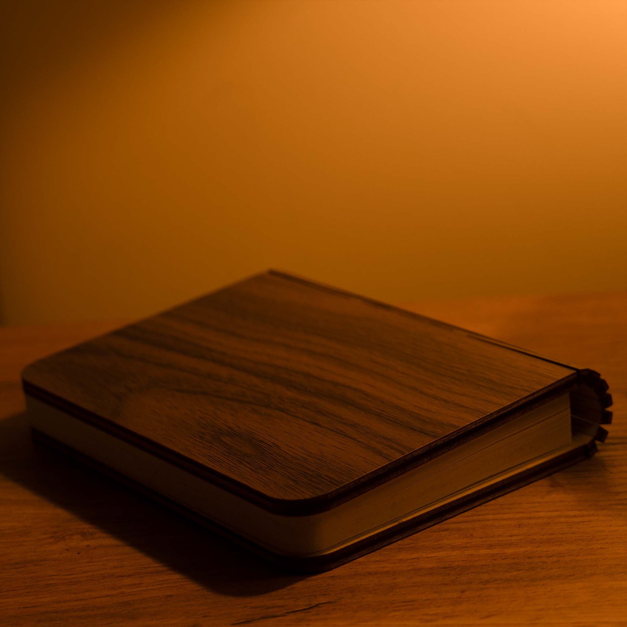 Dark leather-bound book on a wooden surface with a warm, orange-brown background