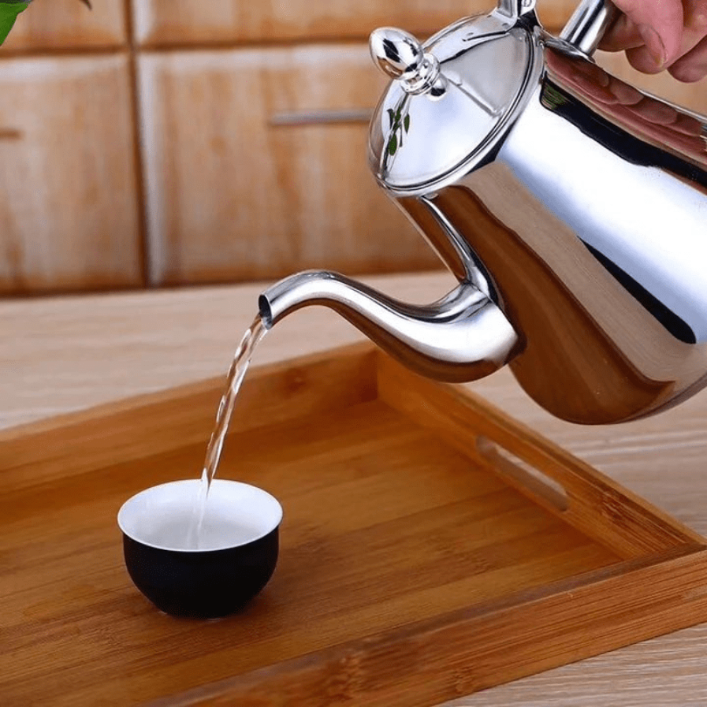 Silver teapot pouring water into a black and white teacup on a wooden surface.