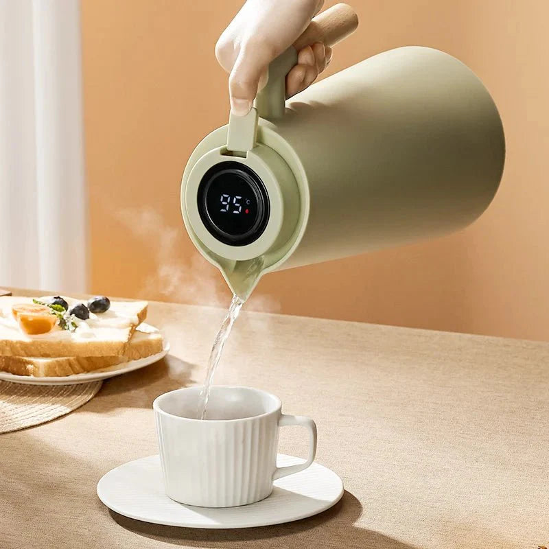 Person pouring steaming hot water from a green electric kettle into a white mug on a wooden table.