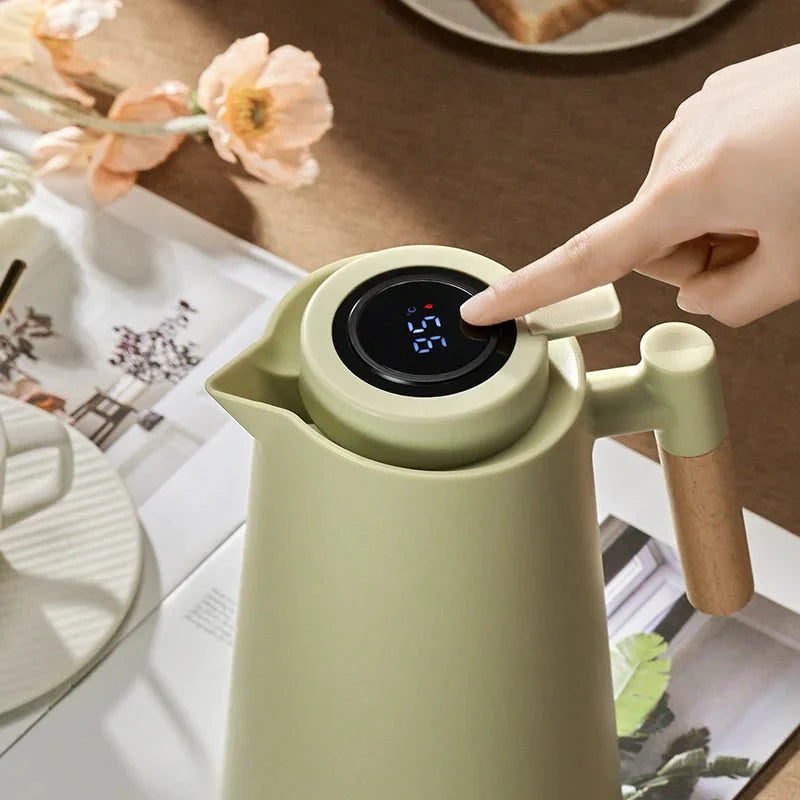 Green electric kettle with digital display on a table with a hand interacting with it.