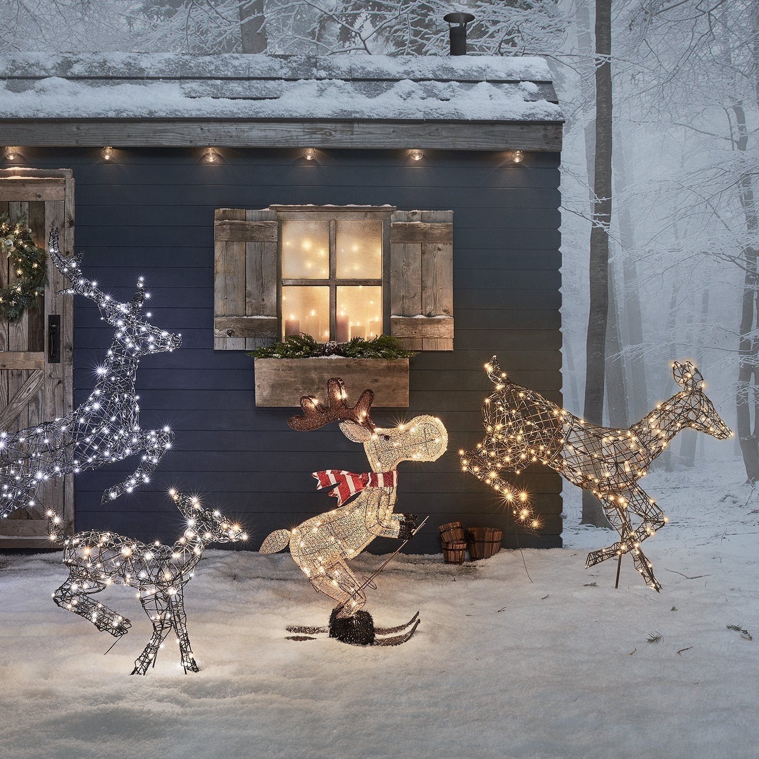 Decorative outdoor scene with illuminated deer figures in front of a snowy cabin.