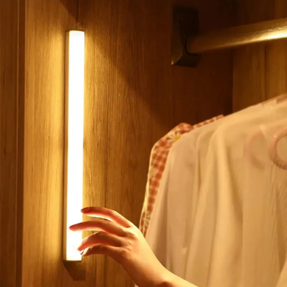Hand turning on a strip light next to a wooden wardrobe with clothes hanging inside.