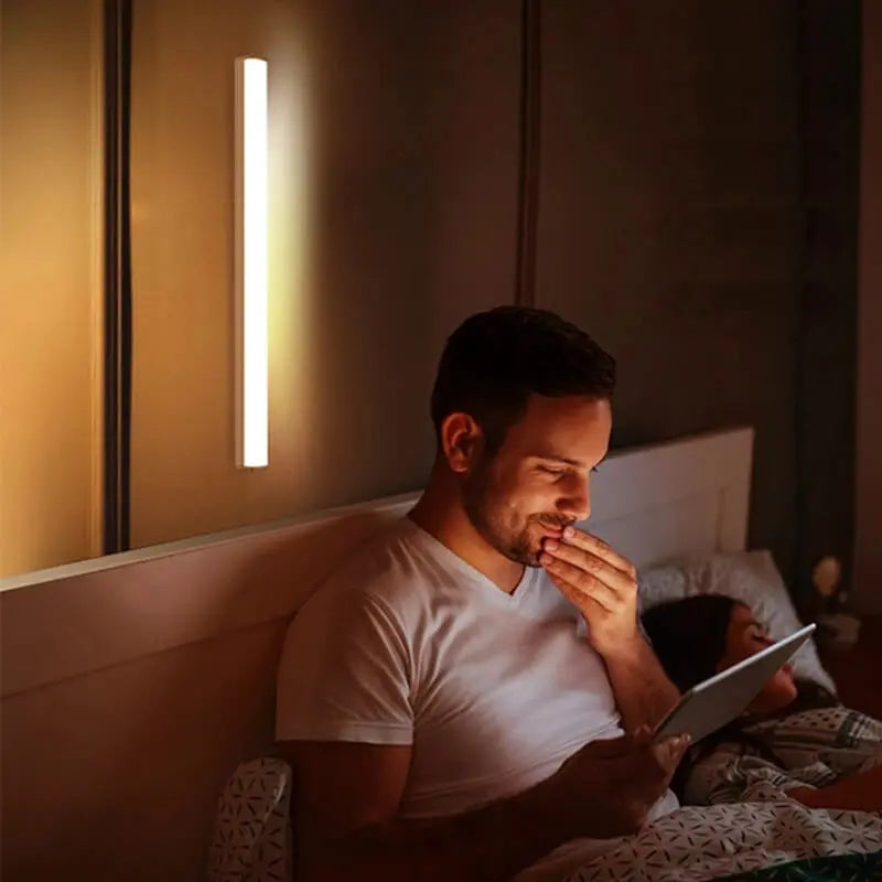 Man sitting on a bed using a tablet with a wall light on in the background