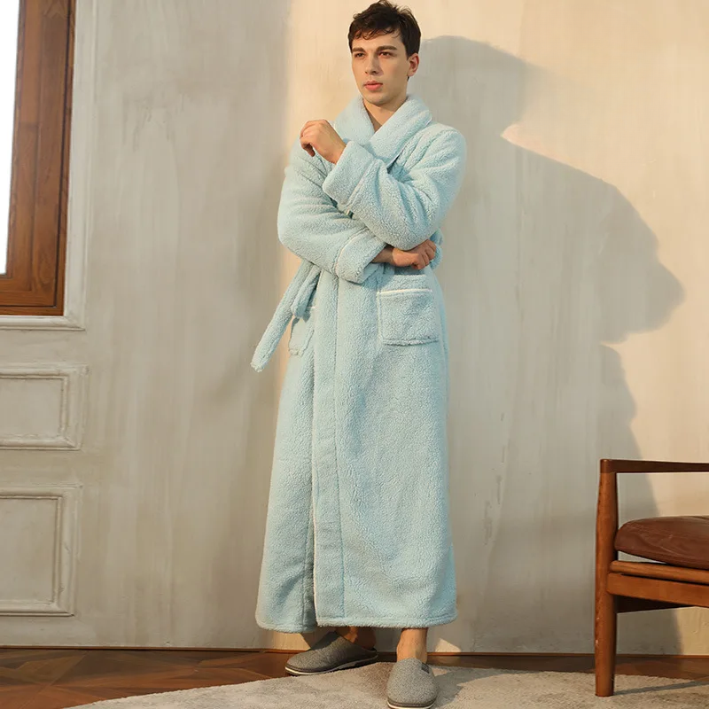 Man wearing a light blue robe standing in a room with a wooden chair and neutral walls.