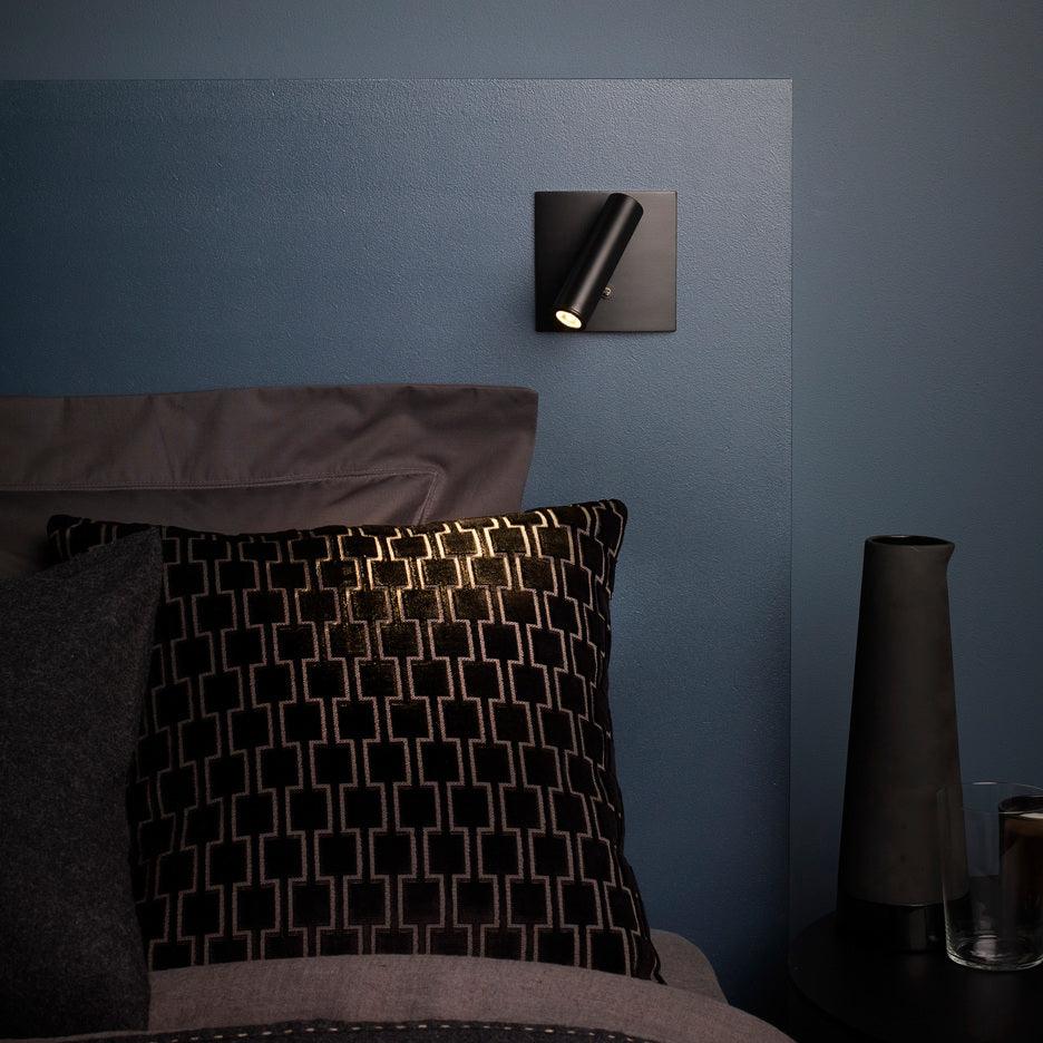 Modern wall light fixture on a blue wall with decorative pillows and a vase.