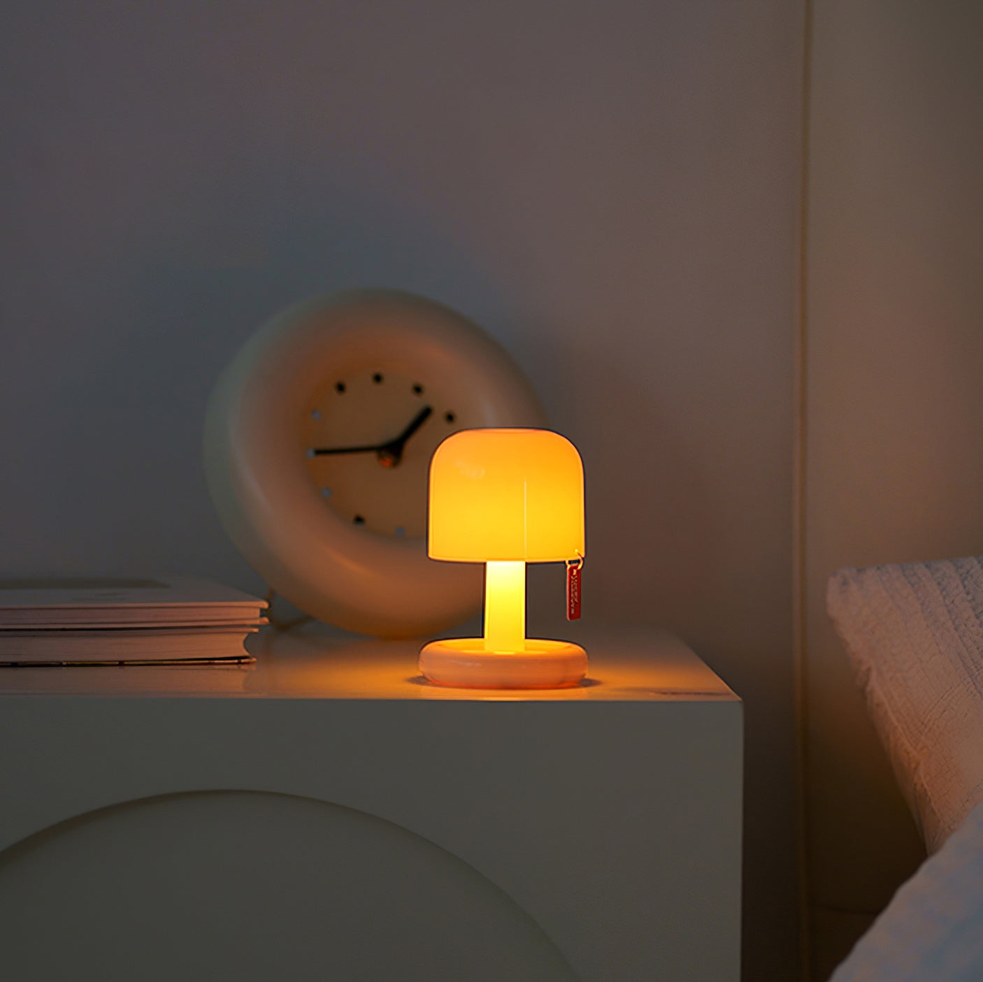 Small lamp on a nightstand with a clock in the background