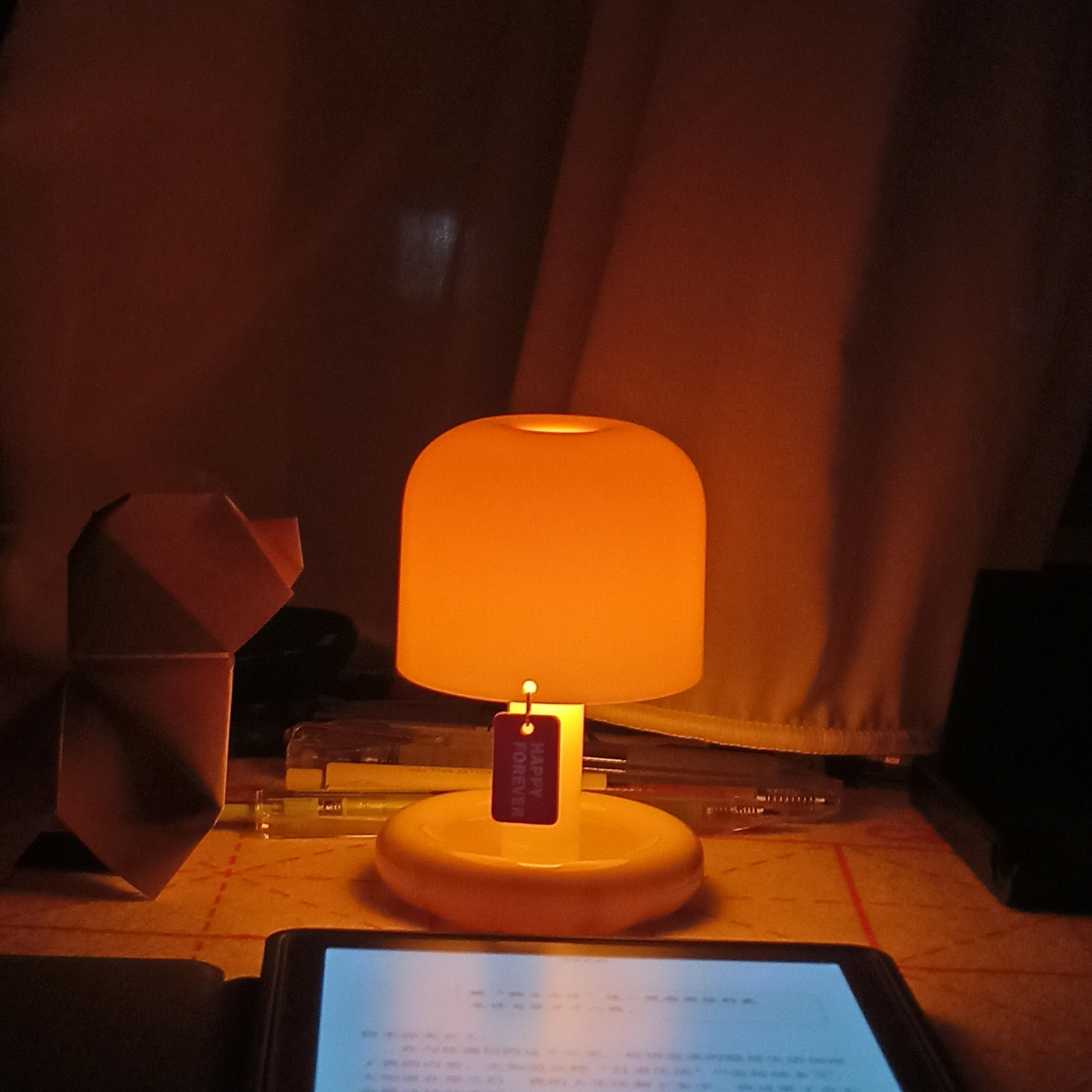 Small round lamp emitting a warm glow on a surface with a tablet in the foreground.