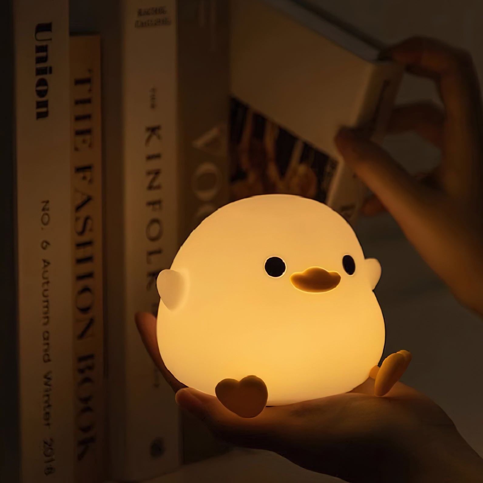 Cute duck-shaped night light held by a hand with books in the background