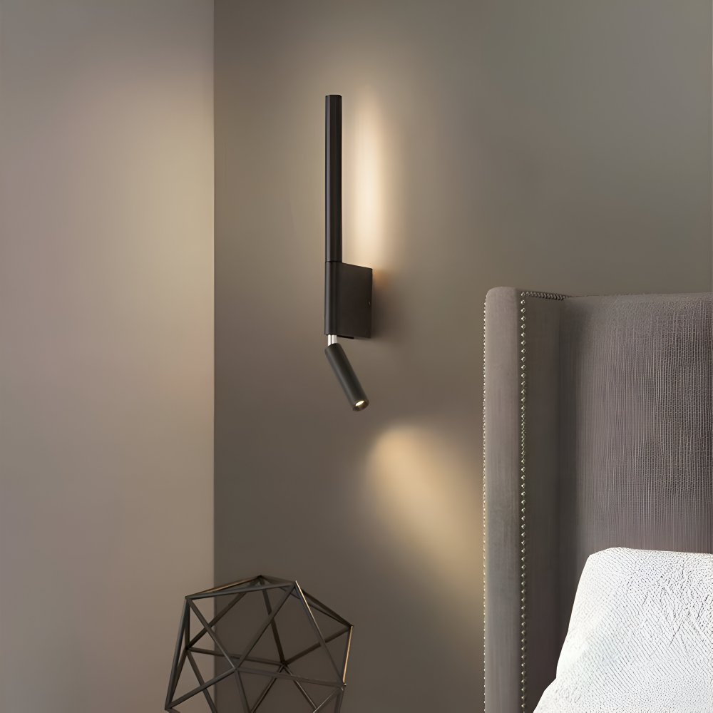 Modern wall-mounted light fixture on a gray wall with a headboard and decorative object in the foreground.