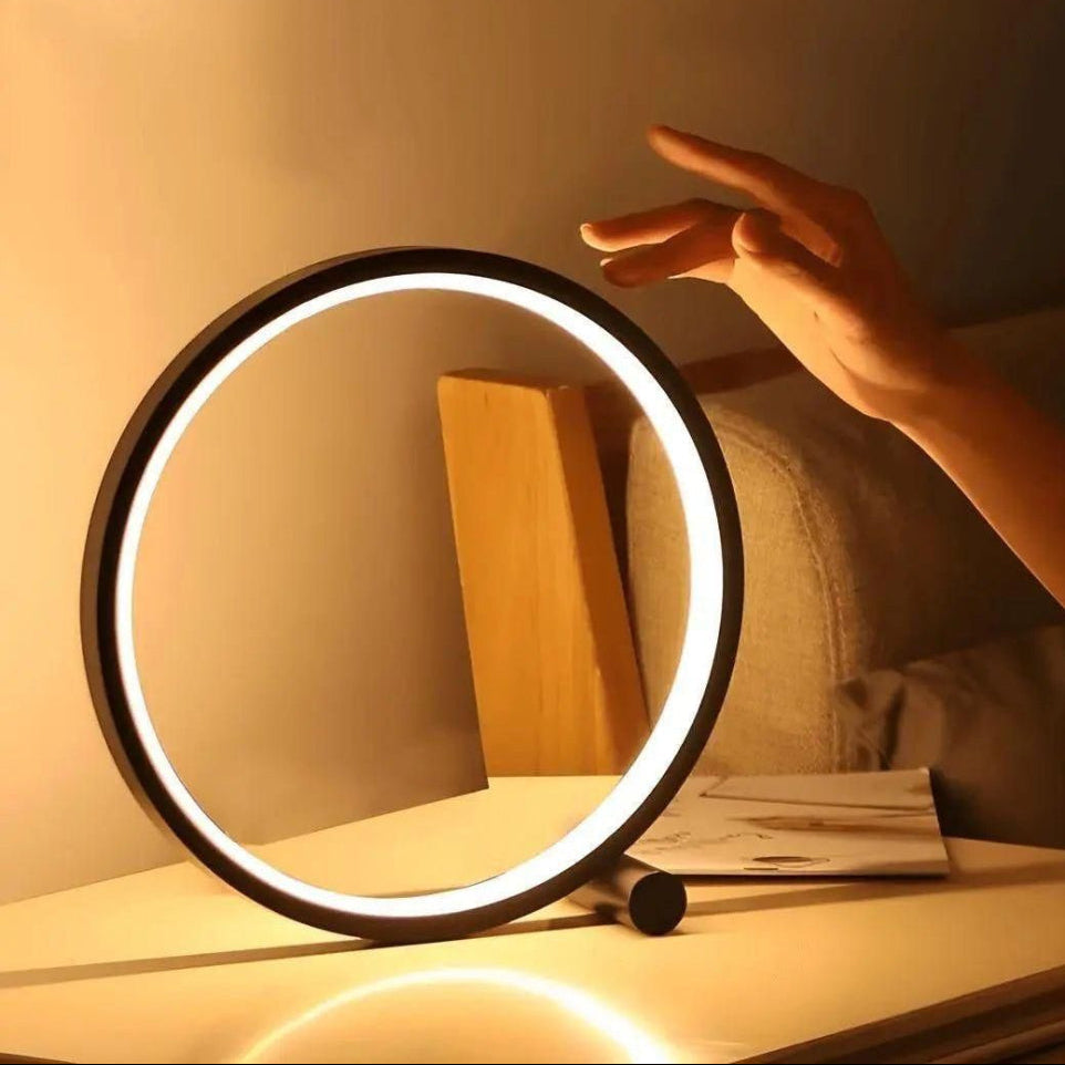 Circular light on a table with a hand reaching towards it, in a warm indoor setting.