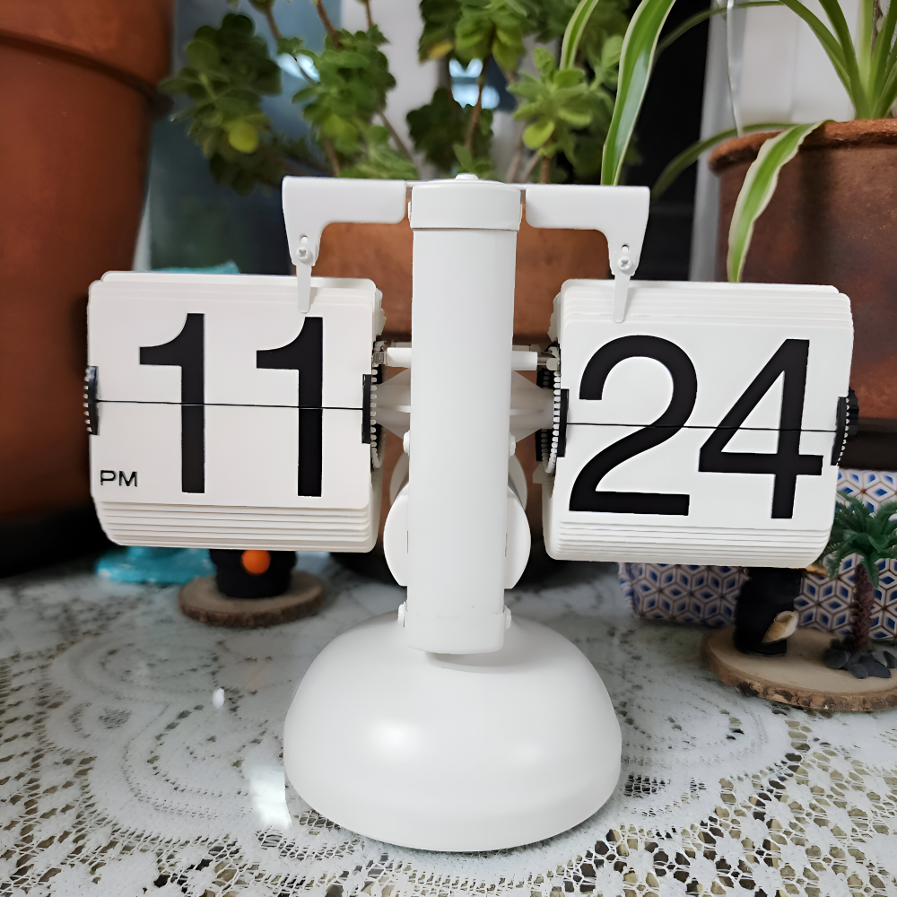 Flipping clock showing 11:24 on a lace tablecloth with plants in the background