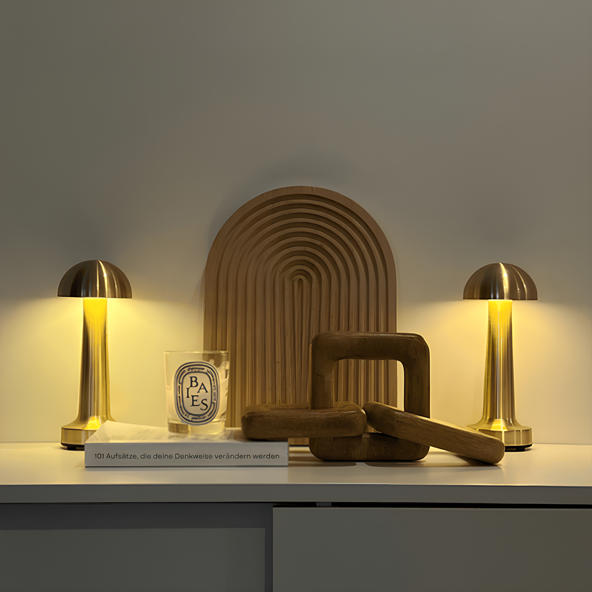 Decorative objects including a brown arch, two gold lamps, and a glass container on a white surface with a gray background.