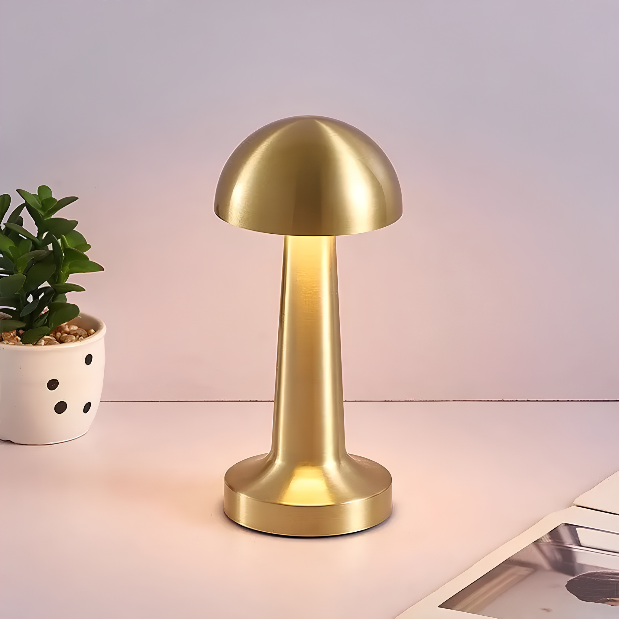 Gold mushroom-shaped table lamp on a light surface with a plant and magazine in the background