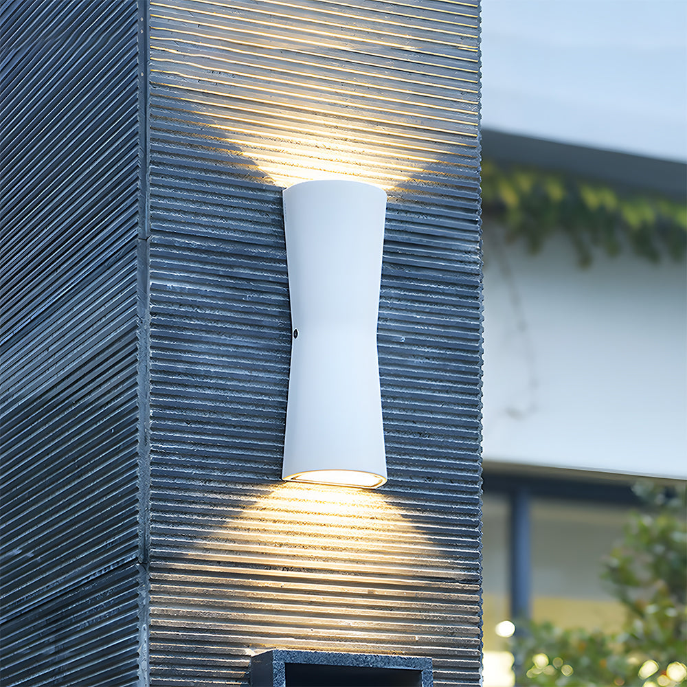 White outdoor wall light fixture on a textured stone wall with blurred background