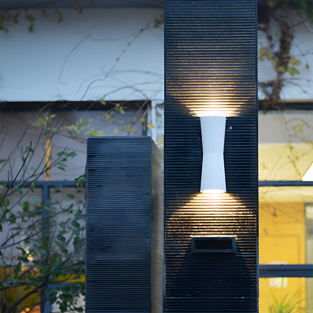 White outdoor wall light fixture on a textured stone wall with blurred background