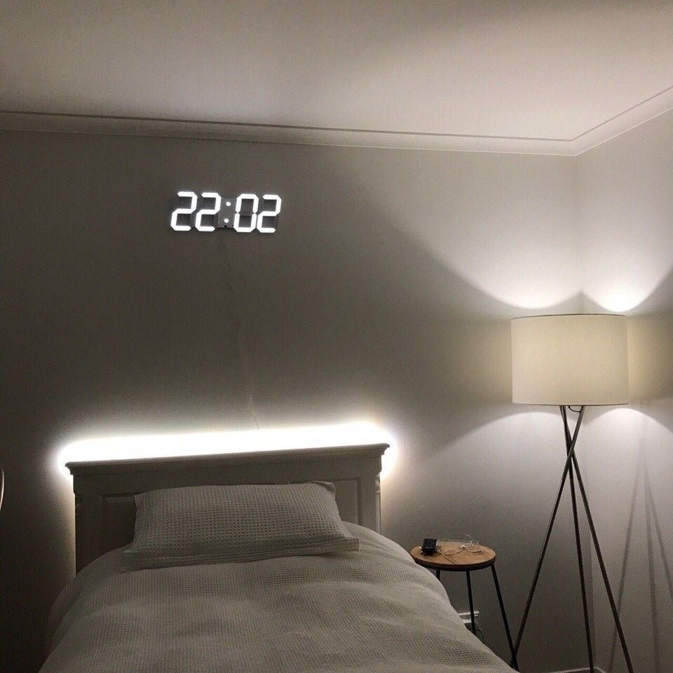 Bedroom with digital clock displaying time on wall, bed, and lamp.