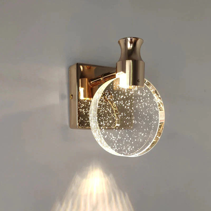 Gold wall sconce with a glass globe shade on a gray wall.