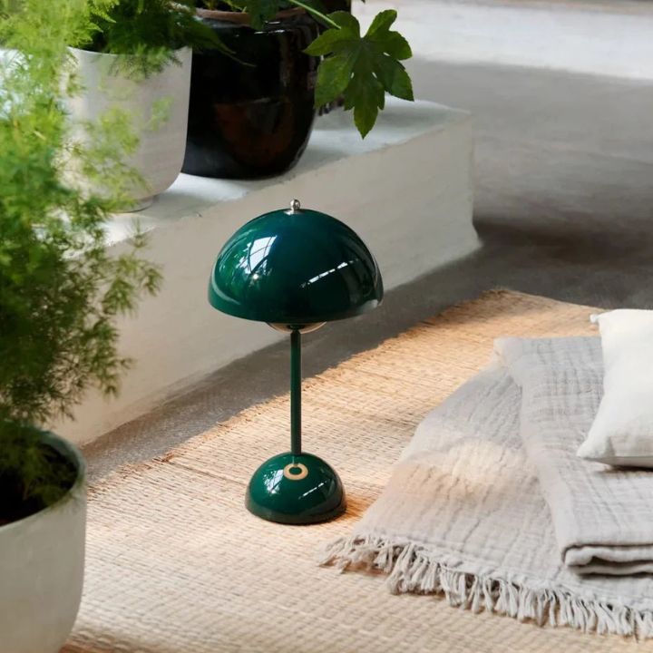 Green table lamp on a textured surface with plants and a white cushion in the background