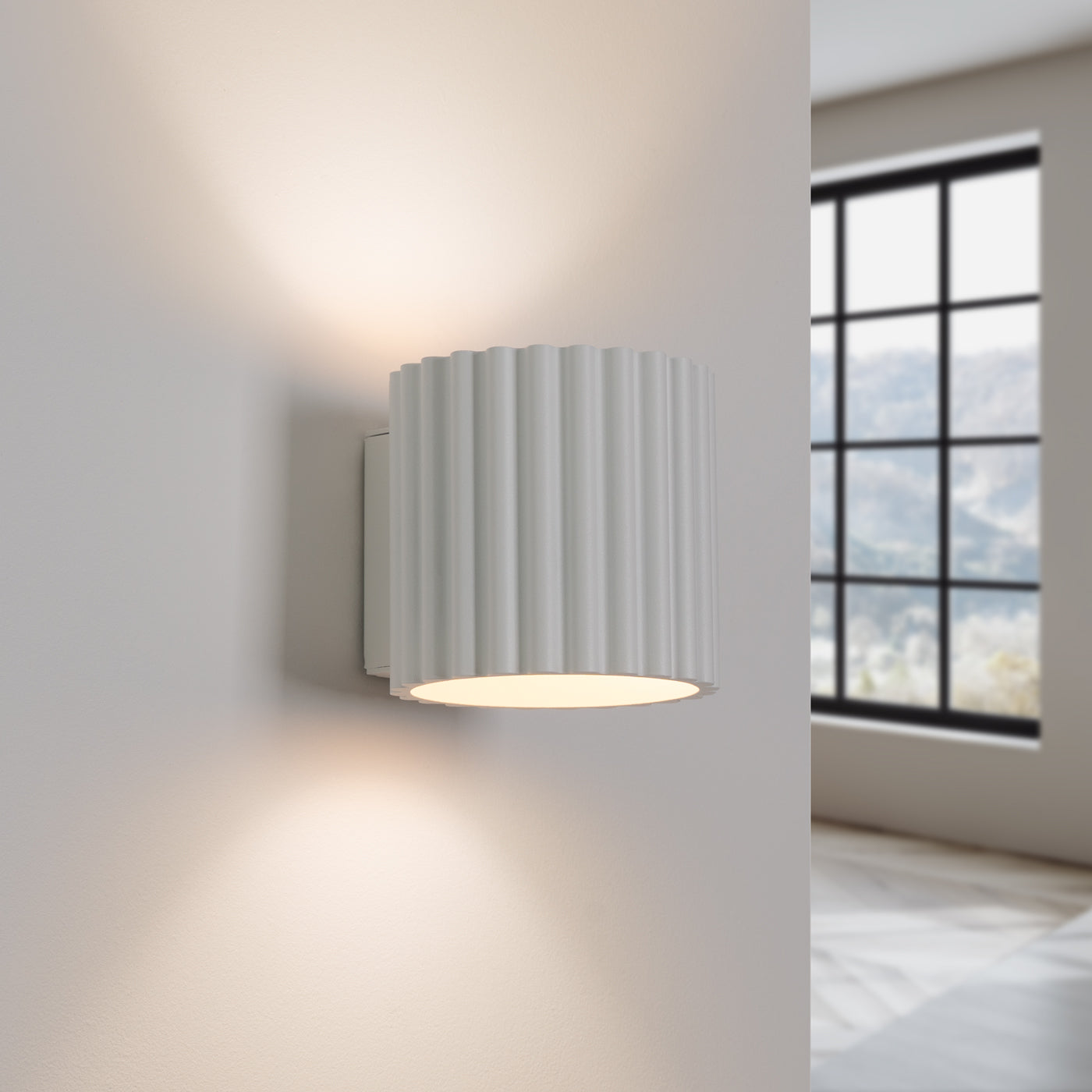 Wall-mounted light fixture with ribbed design on a white wall, room interior visible.