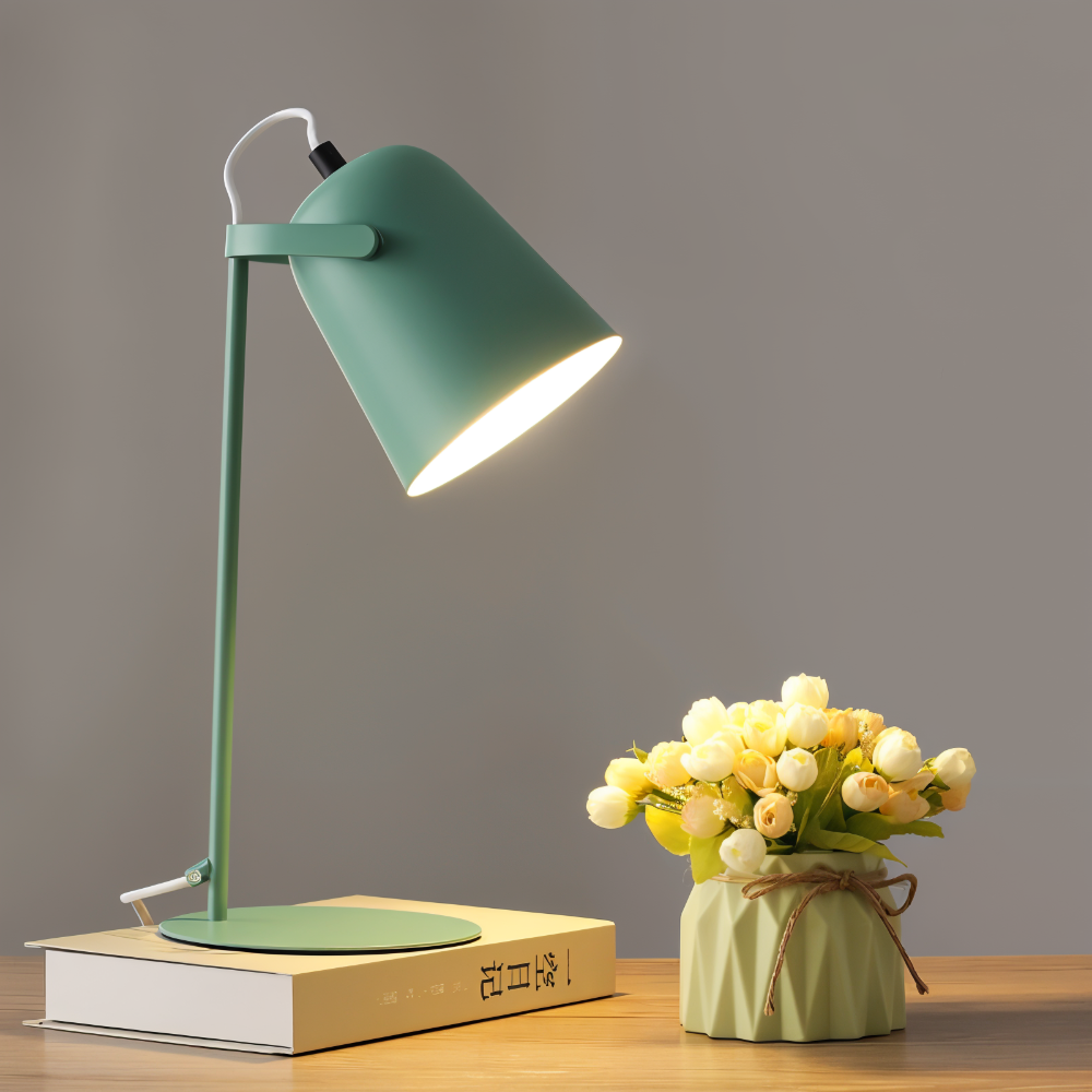 Green desk lamp on a wooden surface with a vase of flowers against a gray background