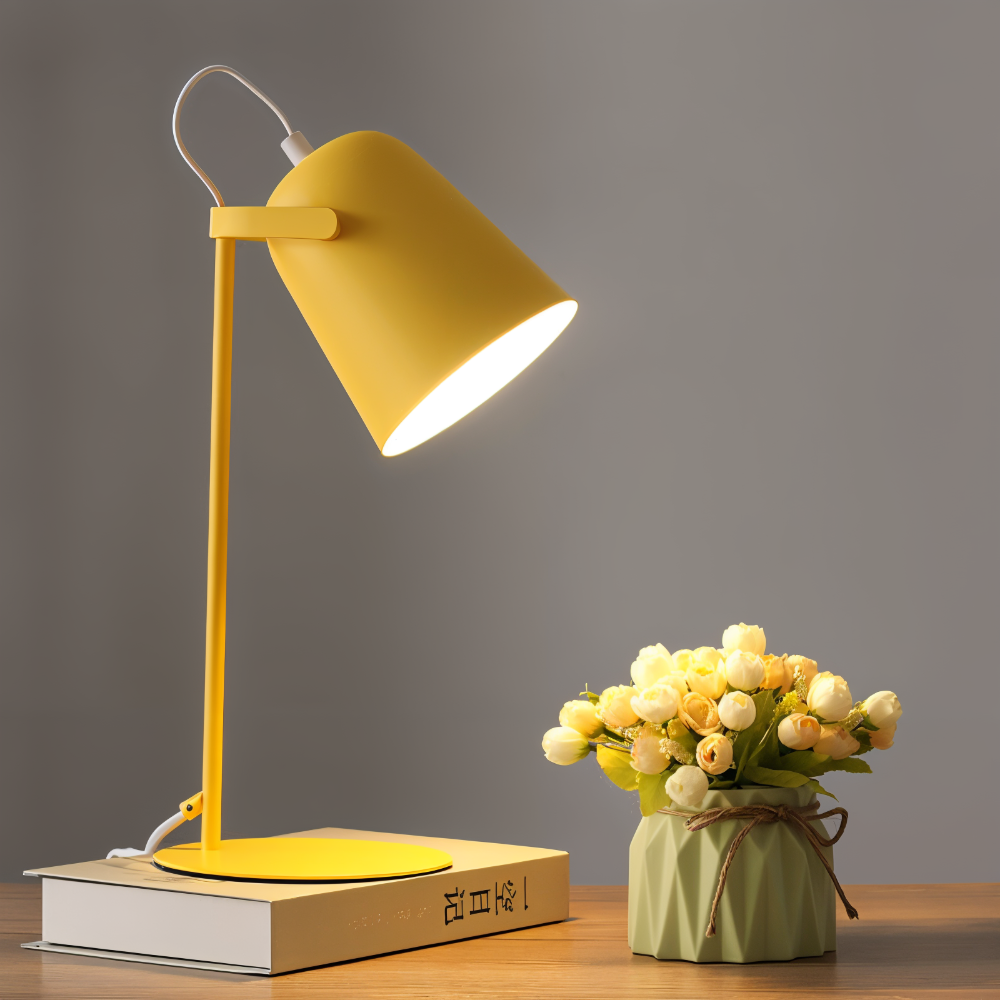 Yellow desk lamp on a book next to a small potted plant on a wooden surface with a gray background
