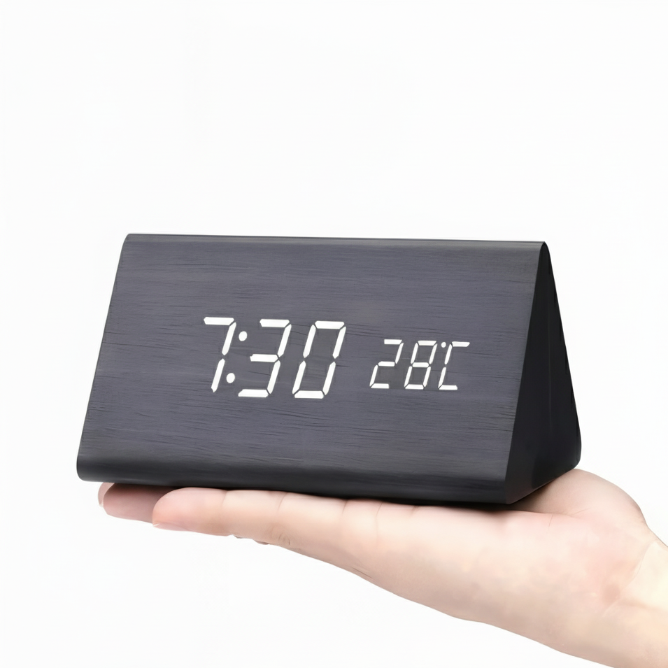 Black digital clock with LED display held in a hand on a white background