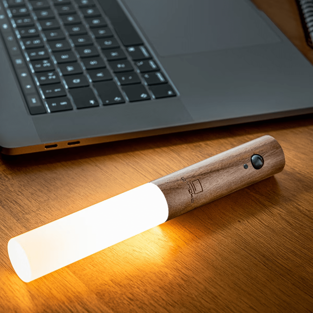 Wooden-handled flashlight on a wooden desk with a laptop in the background