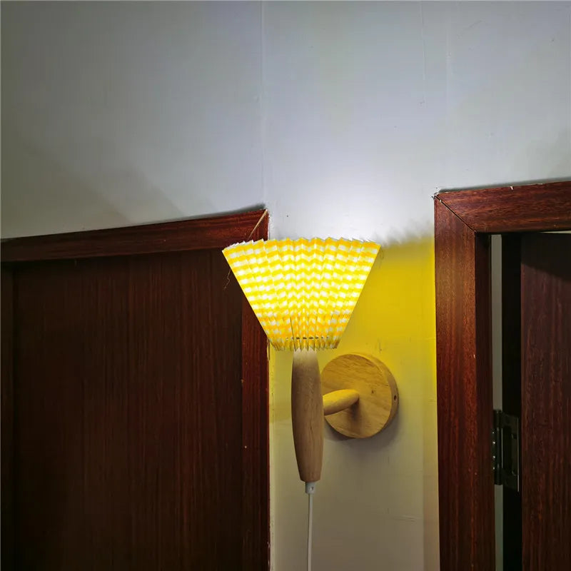 Wall-mounted lamp with yellow shade and wooden base on a white wall.