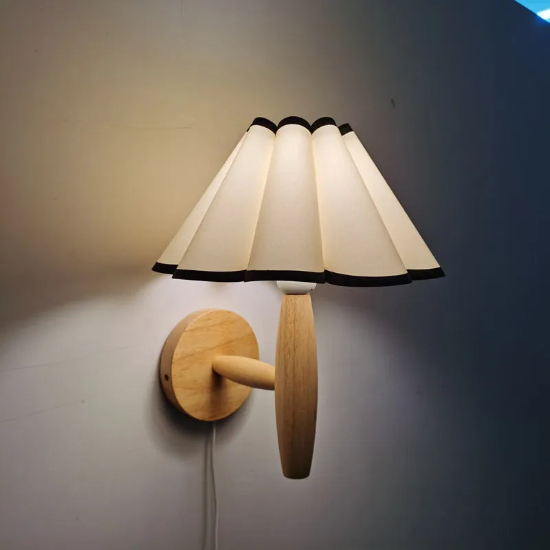Wall-mounted lamp with pleated white shade and wooden base on a gray wall.