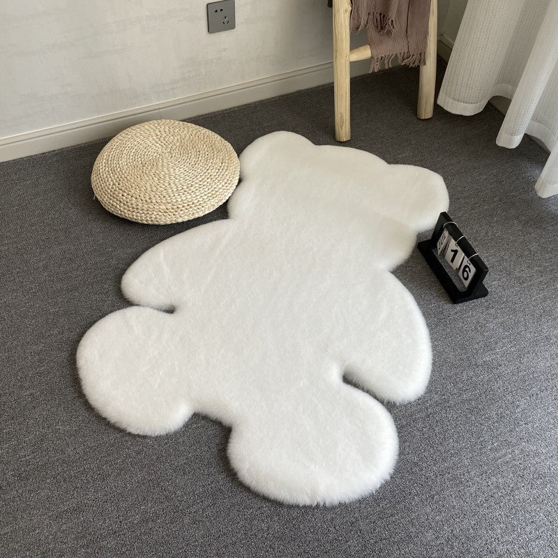 White teddy bear-shaped rug on a gray carpet with a small stool and bag in the background.