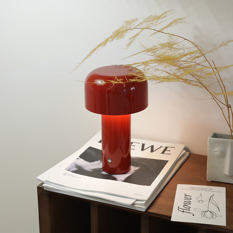 Red table lamp on a magazine with a vase of dried plants in the background