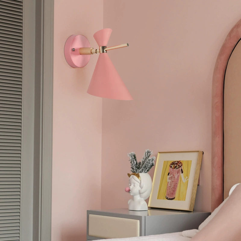 Pink wall lamp on a pink wall with decorative items on a shelf.