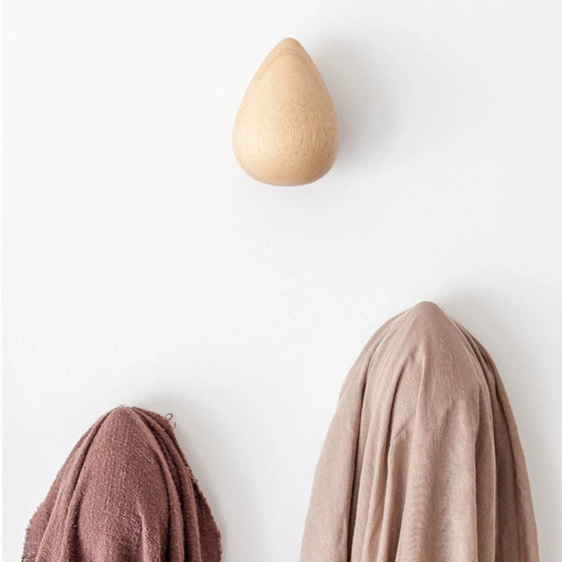 Wooden teardrop-shaped hook with fabric draped over it on a white wall