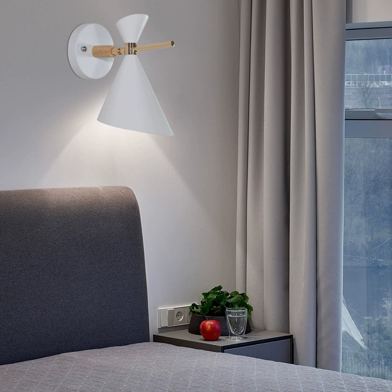 Modern wall lamp on a gray wall above a bed with a nightstand and decorative items.