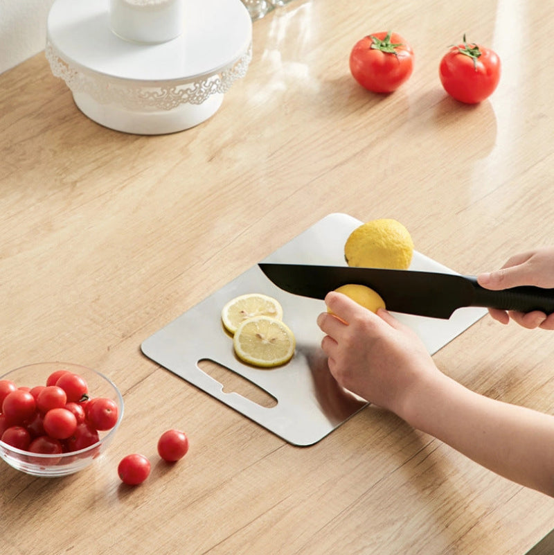 Person slicing lemons on a cutting board with a knife, surrounded by fruits on a wooden table.
