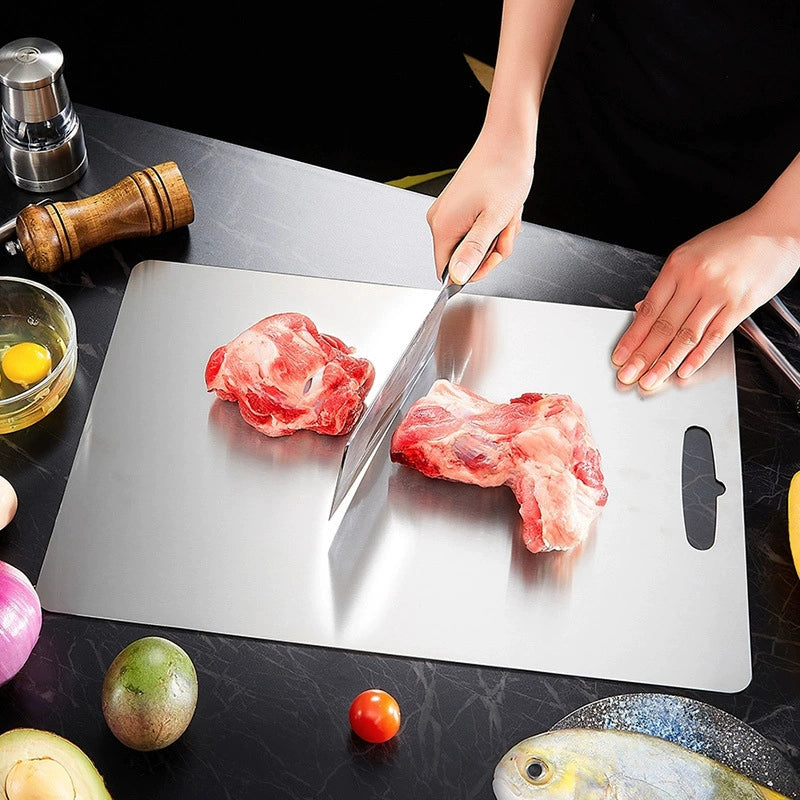 Person cutting raw meat on a metal cutting board with a knife.