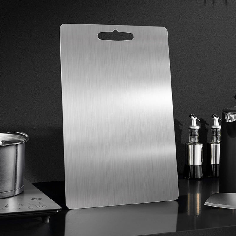 Metallic cutting board on a dark surface with kitchen items in the background
