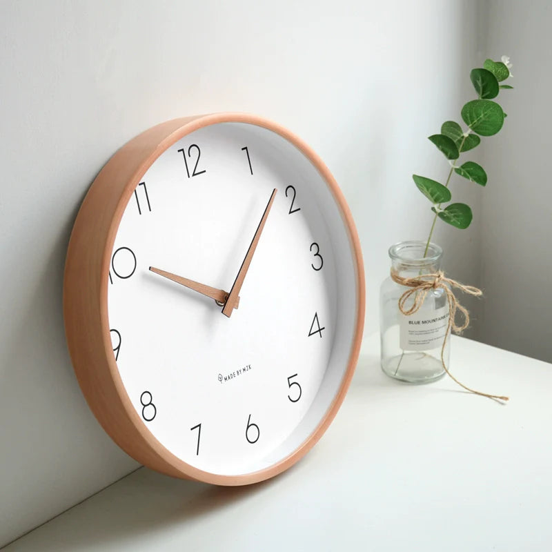 Wall clock with wooden frame on a white wall next to a vase with greenery